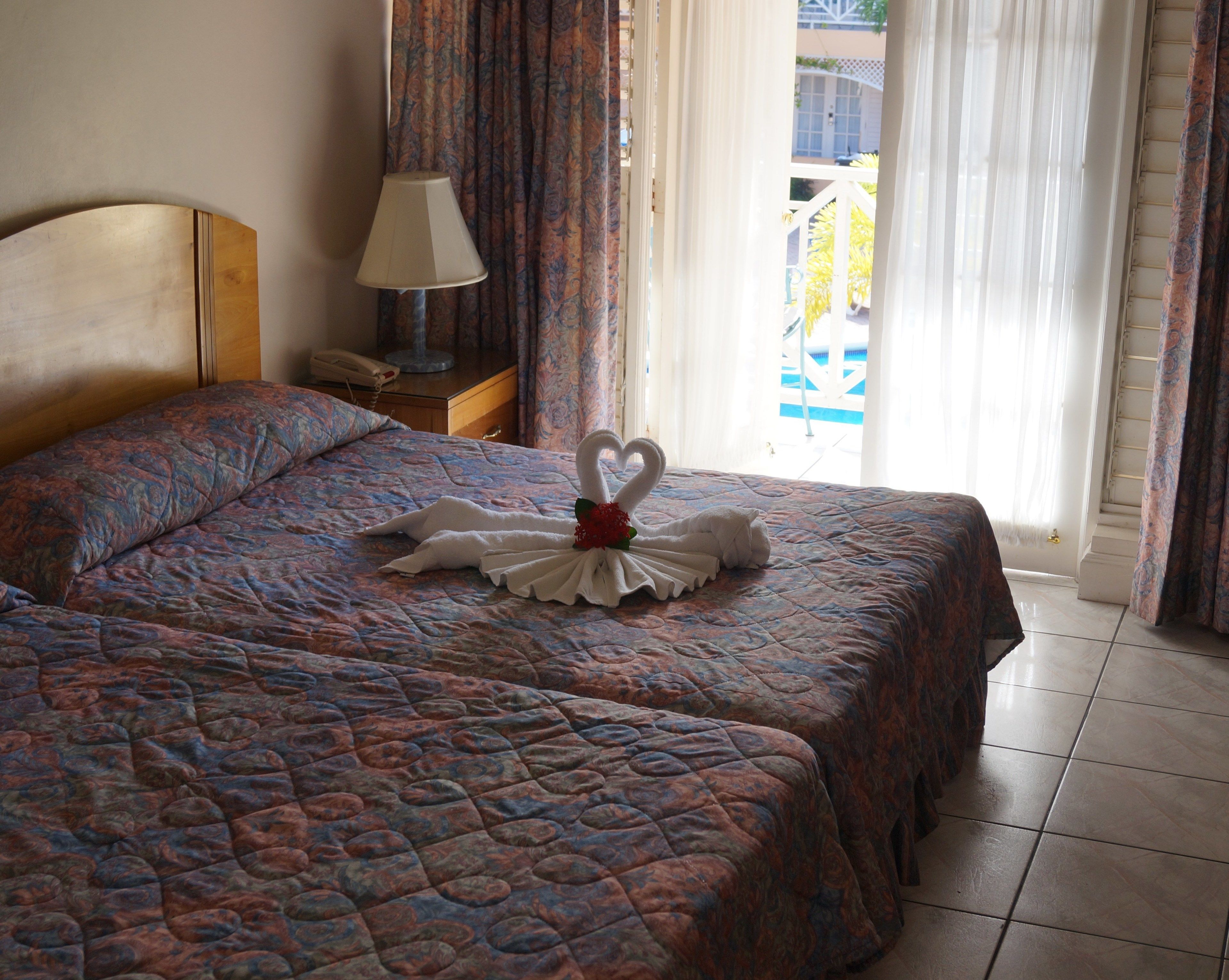 A hotel room with a bed featuring a decorative swan towel arrangement, a bedside lamp, and a view of the outside balcony.