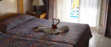 Habitación de hotel con una cama que presenta una decoración de toallas en forma de cisne, una lámpara de noche y vistas al balcón exterior.