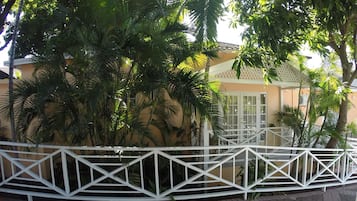 A building with a white fence, surrounded by lush greenery and palm trees.