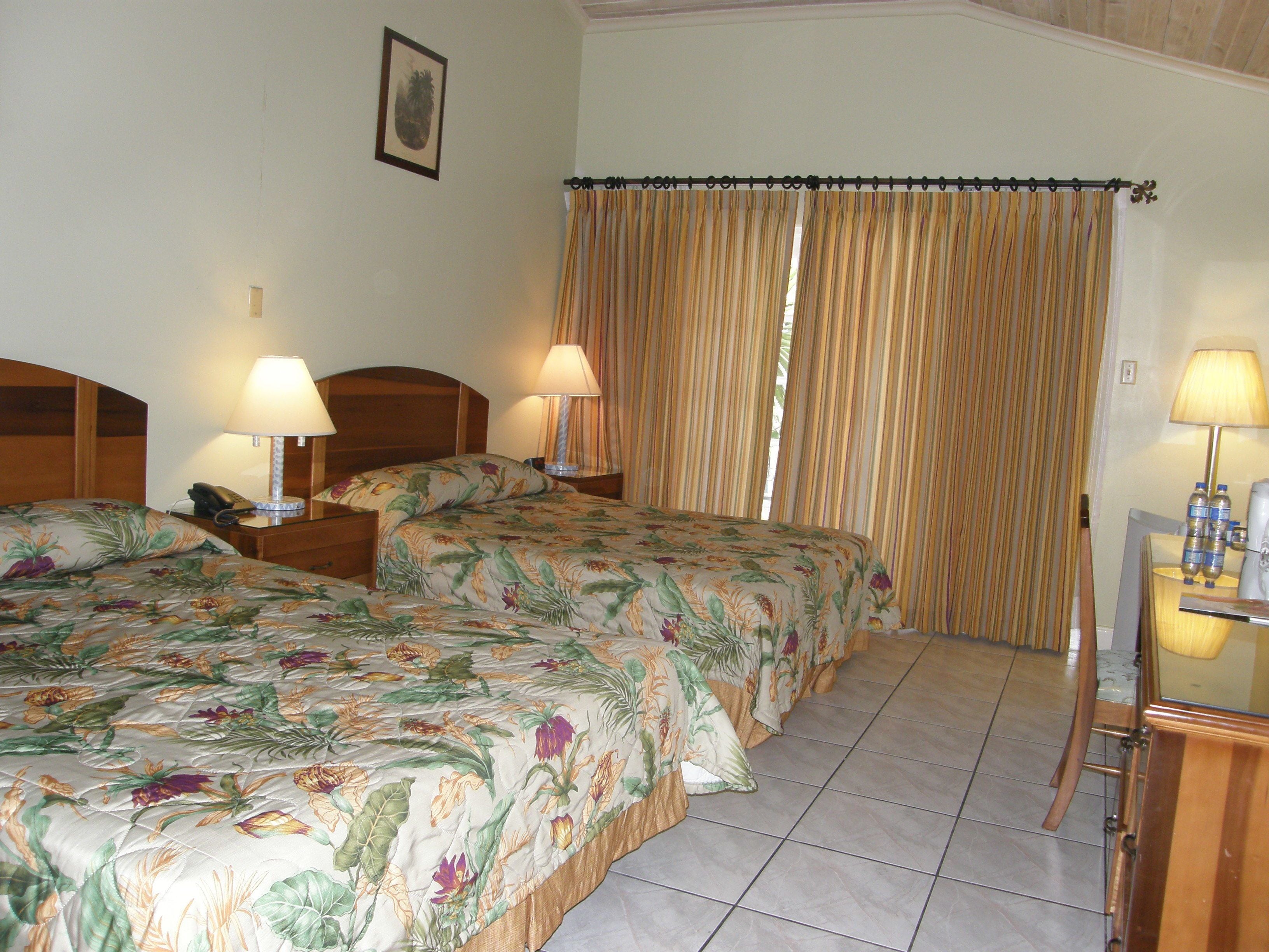 A hotel room with two beds, a desk with a chair, and a window with curtains.