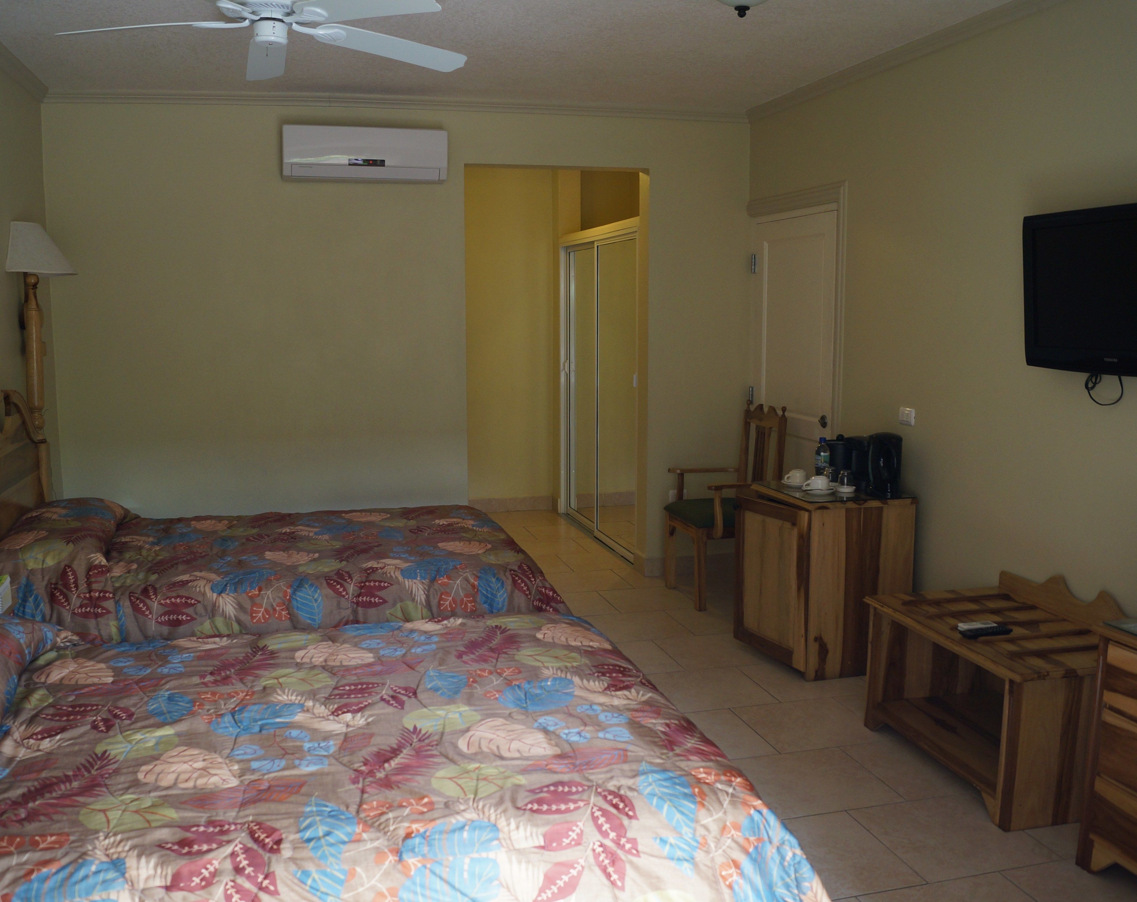 A bedroom with a bed, a desk, a chair, a television, and an air conditioning unit.