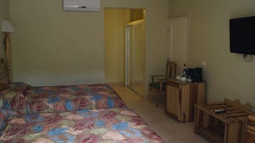 A bedroom with a bed, a desk, a chair, a television, and an air conditioning unit.
