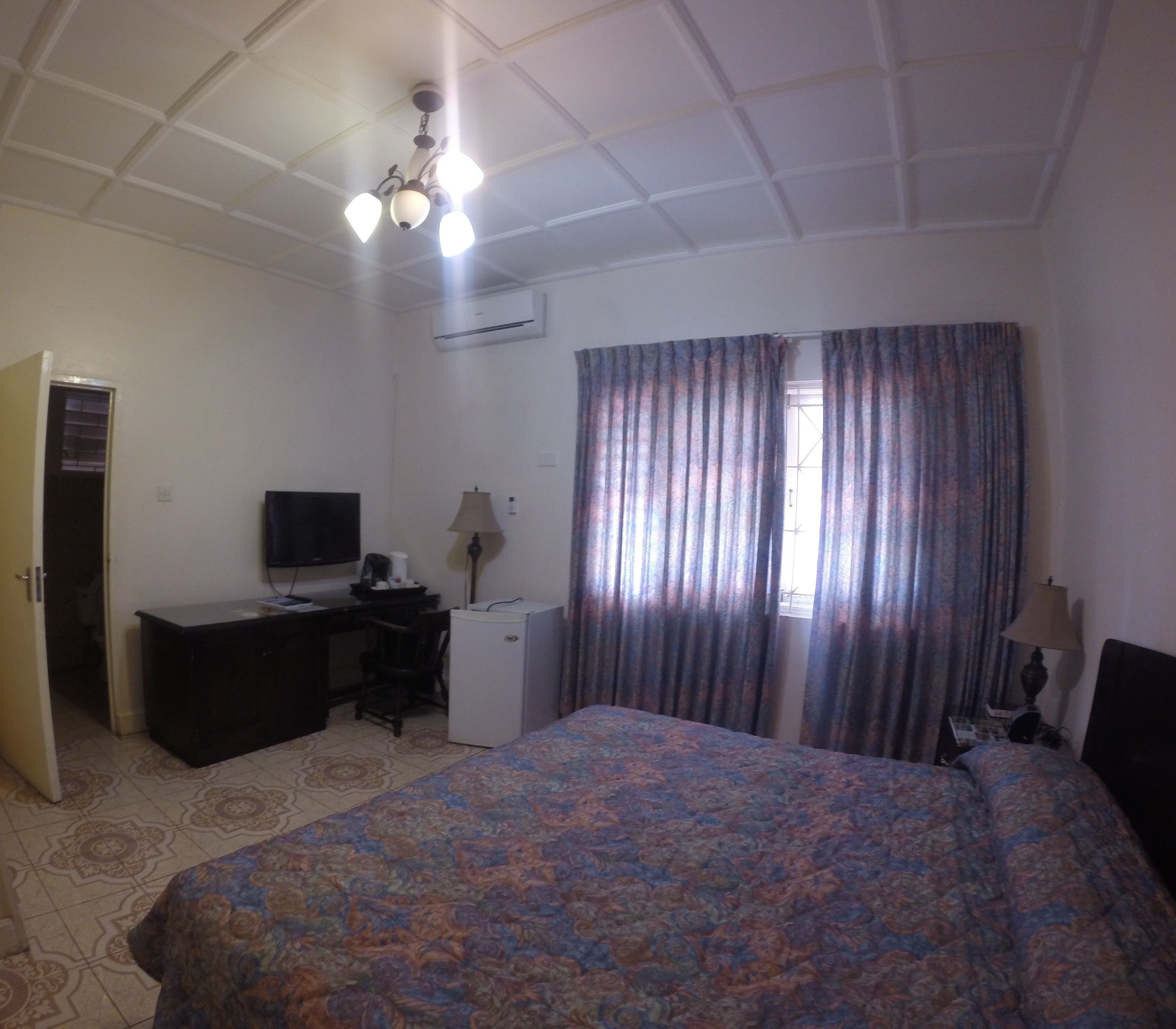 Un dormitorio con cama, escritorio, televisor y refrigerador.