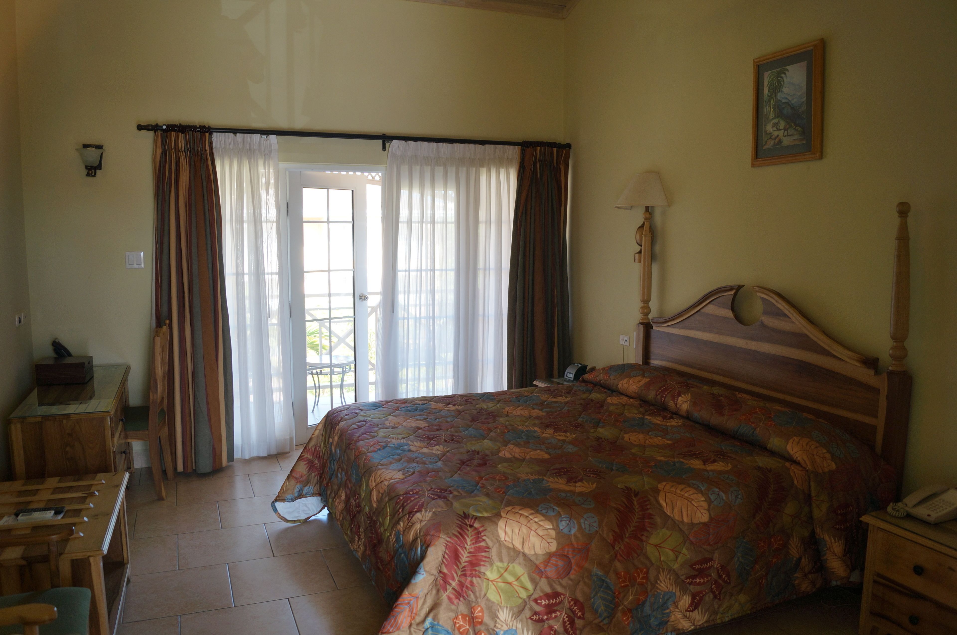 Une chambre à coucher avec un lit, un bureau, une chaise, une lampe et une porte avec des rideaux.