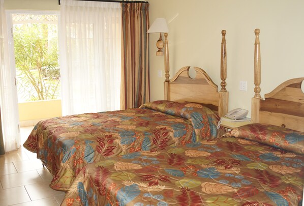 Uma cama de casal com colcha florida, mesa de cabeceira com abajur e telefone.