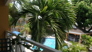 A balcony with a view of a swimming pool surrounded by palm trees and a building with a tiled roof. - Hotel Four Seasons (Kingston)