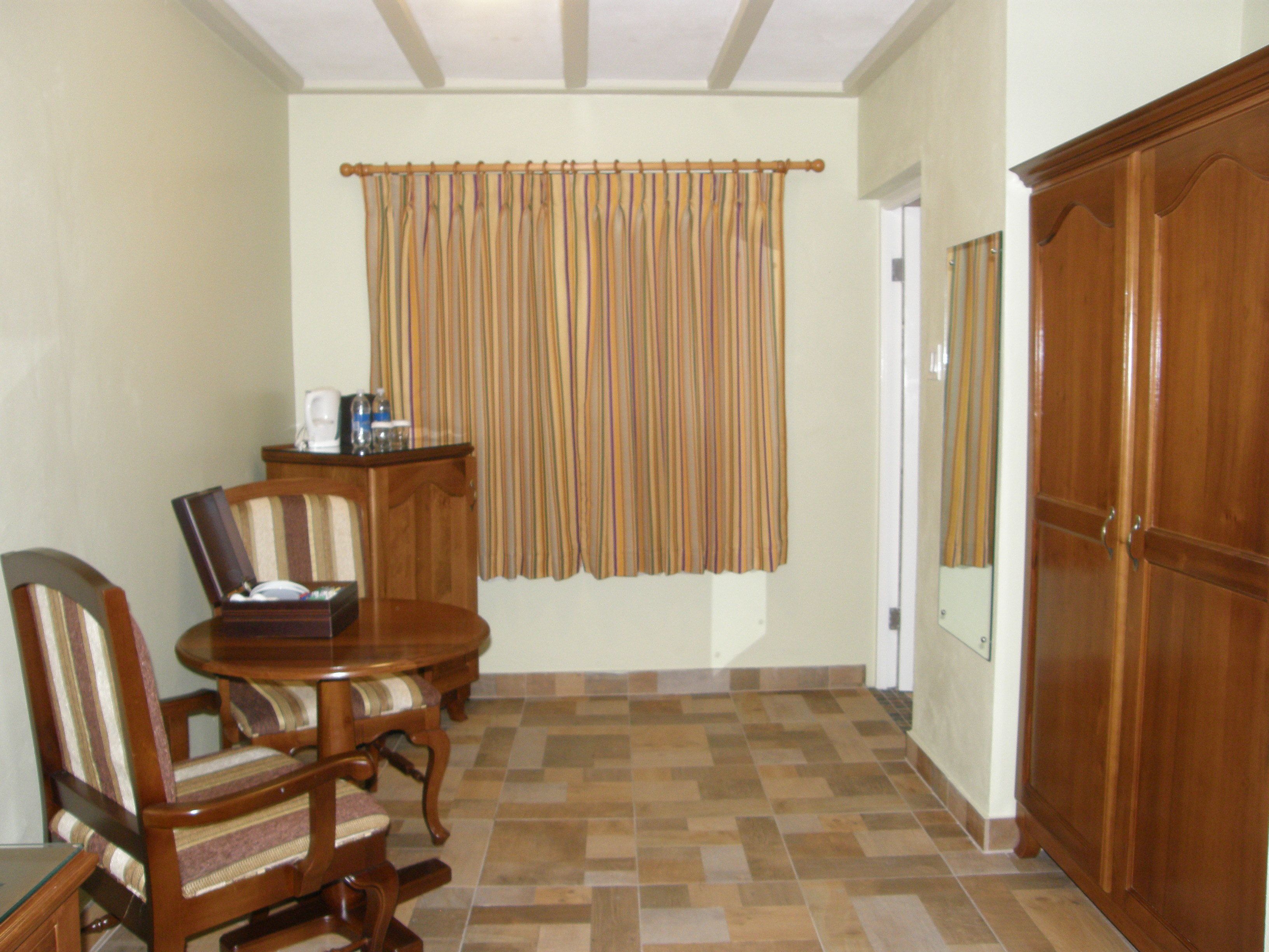 A dining area with a wooden table and chairs, a window with striped curtains, and a wooden wardrobe.