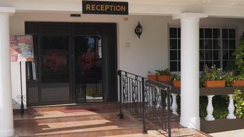 A reception area with a sign, steps leading up to the entrance, and potted plants on the porch.
