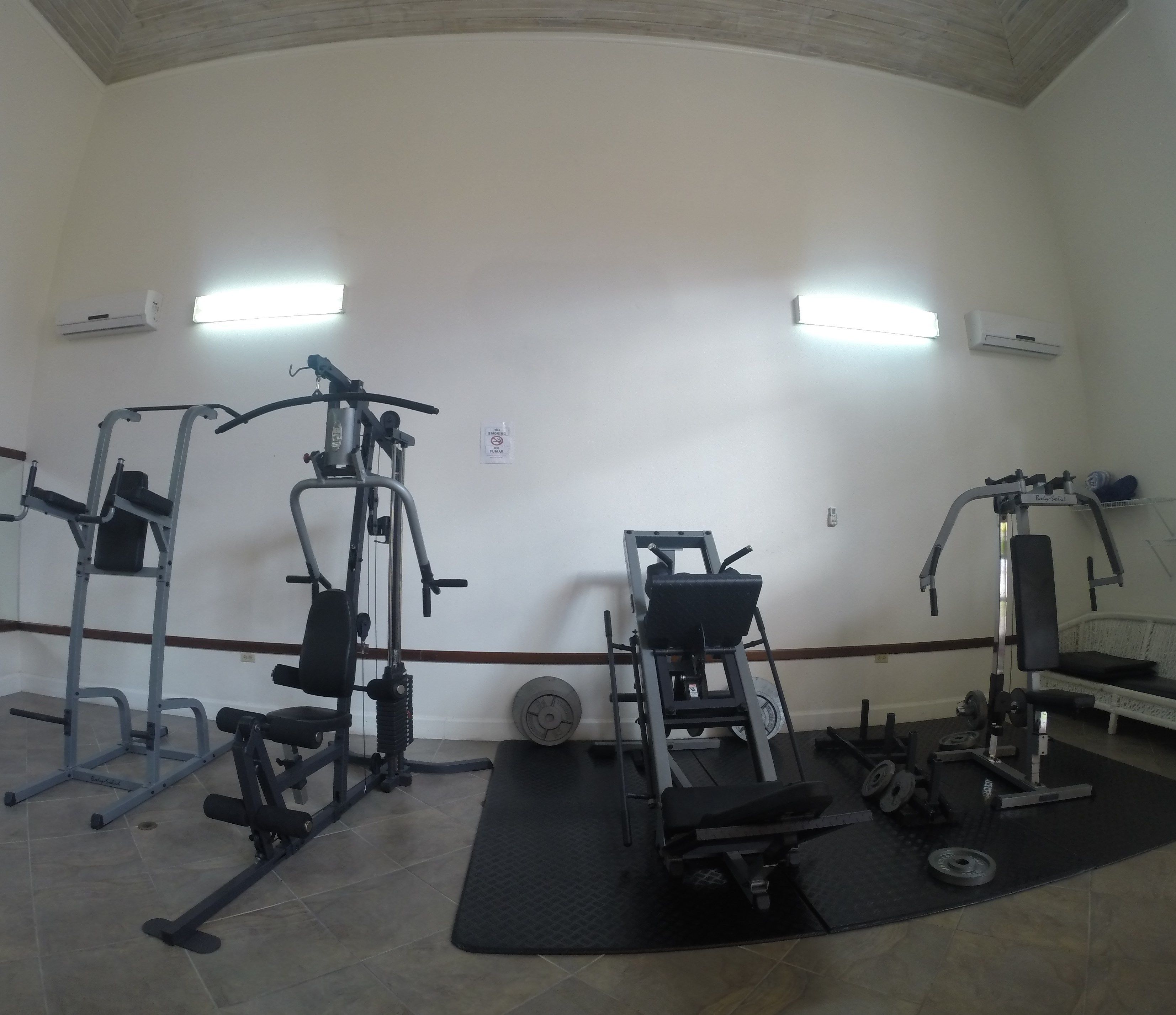 Un gimnasio con diversos equipos de ejercicio, una banca y un aire acondicionado instalado en la pared.