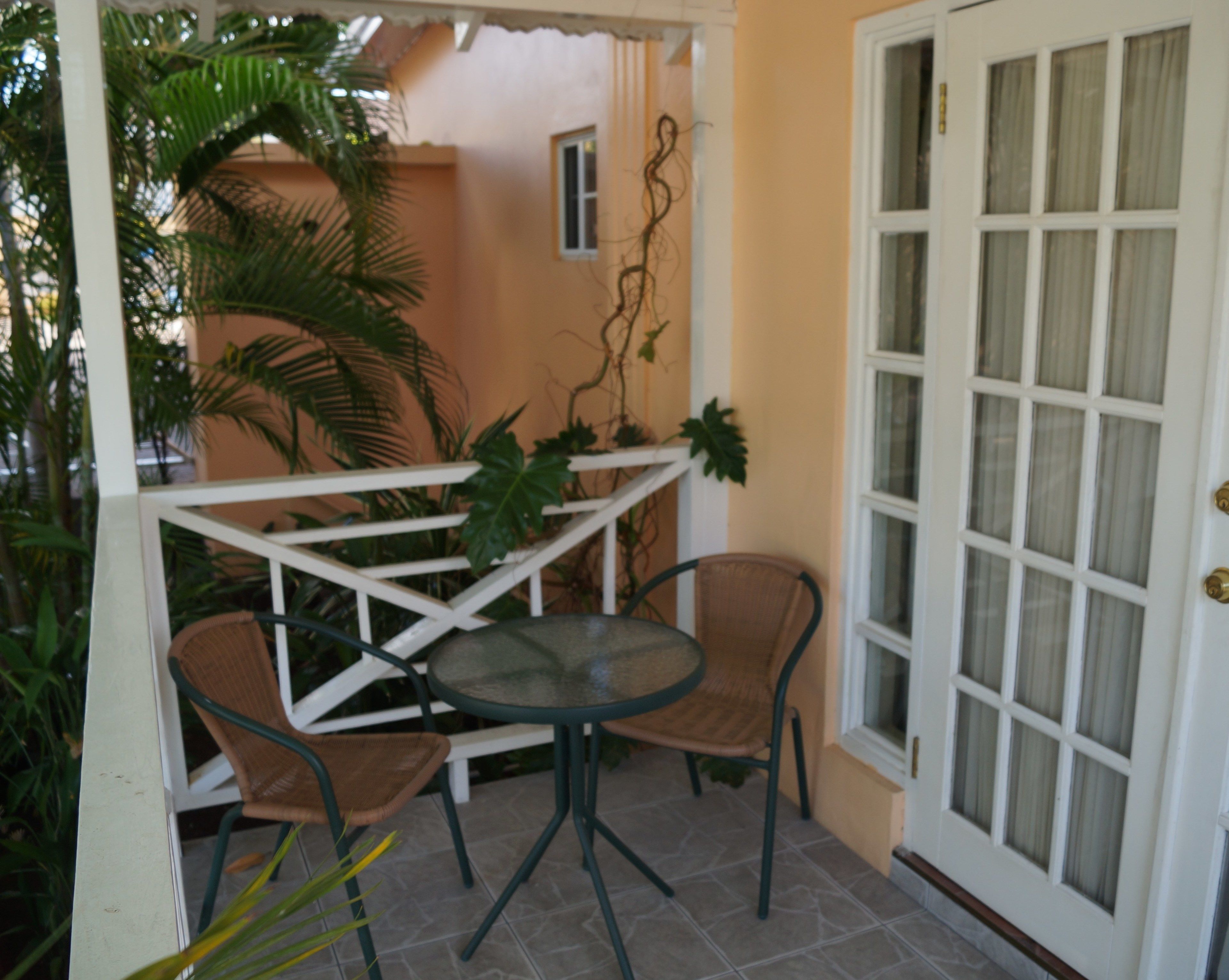 A patio with a round table and two wicker chairs, a white door with glass panels, and a small window.