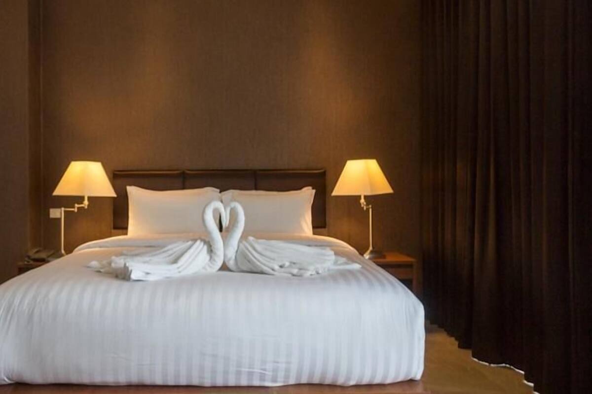 A hotel room with a large bed, two bedside lamps, and a heart-shaped towel arrangement on the bed.