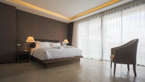 Ein modernes Hotelzimmer mit einem großen Bett, zwei Nachttischlampen, einem Sessel und einem großen Fenster mit durchsichtigen Vorhängen.