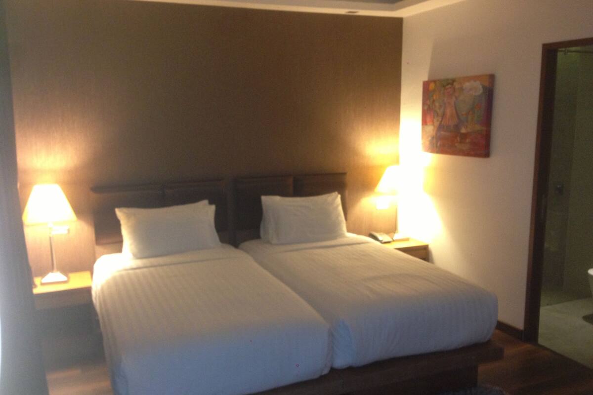 A double bed with white linens, two bedside tables with lamps, and a painting on the wall.
