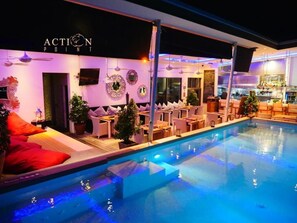 Zona junto a la piscina con sillas de descanso, un bar y un letrero que dice 'ACTION POINT'.