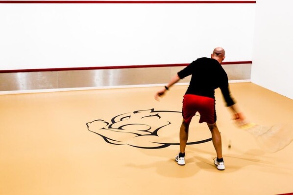 Una persona jugando squash en una sala con un logotipo grande en el suelo.