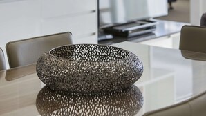 A modern kitchen with white cabinetry, a dining table with a woven centerpiece, and a fruit bowl on the counter. - Oaks Mackay Carlyle Suites (Mackay)