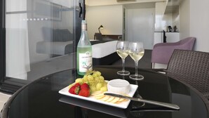 A dining table with a bottle of Jacob's Creek wine, two glasses of white wine, a plate of strawberries, grapes, and cheese, and a knife. - Oaks Mackay Carlyle Suites (Mackay)