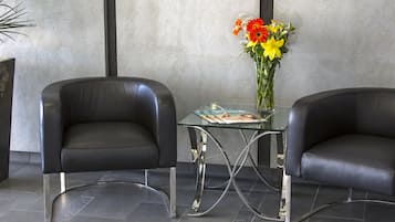 Two black leather chairs with metal legs, a glass table with a magazine, and a vase with flowers.