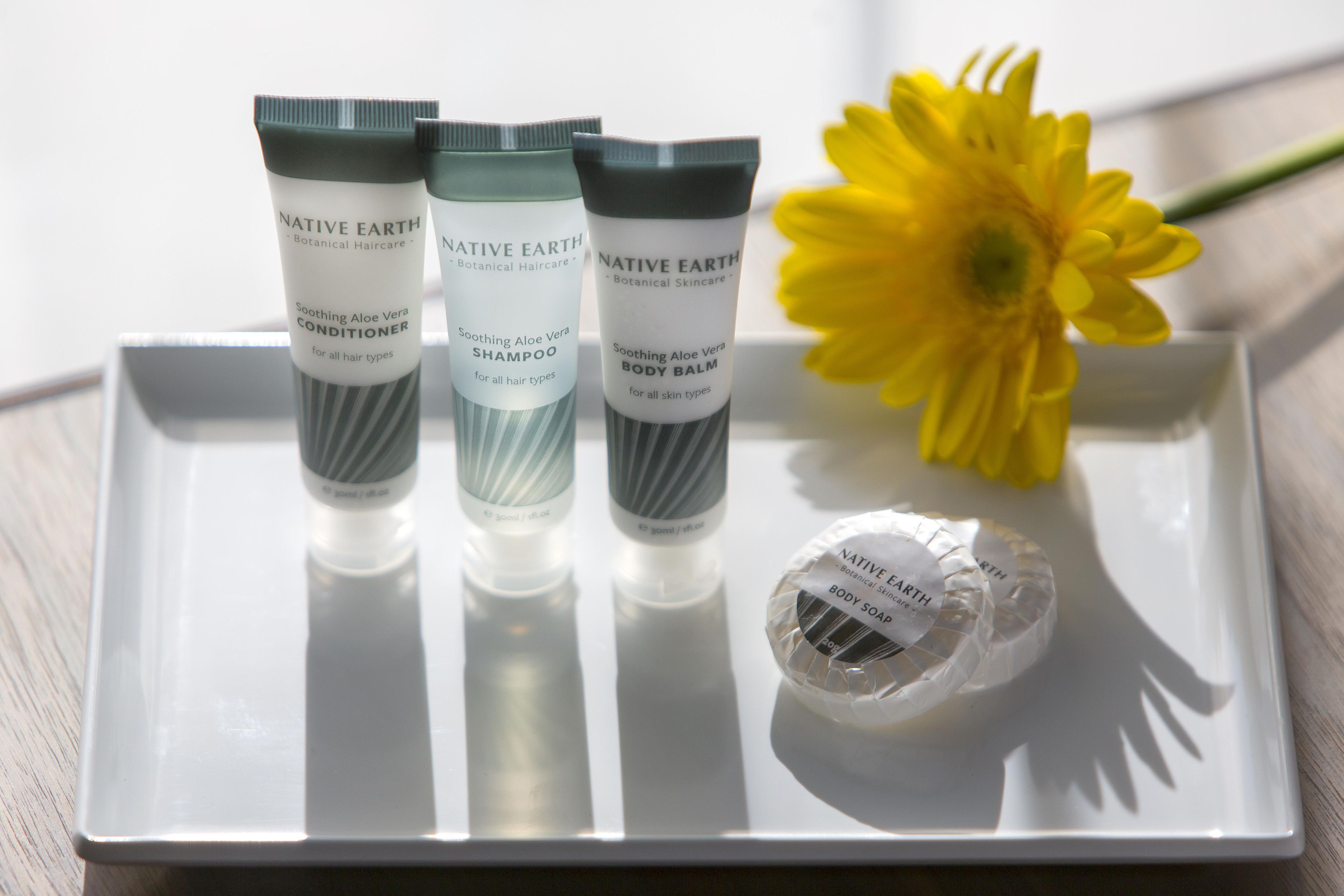 Three tubes of Native Earth Botanical Haircare on a white tray with a yellow flower and a body soap.