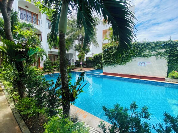 A swimming pool surrounded by lush greenery and a white building with balconies. - Dong Xuan Hong Hotel (Phu Quoc)