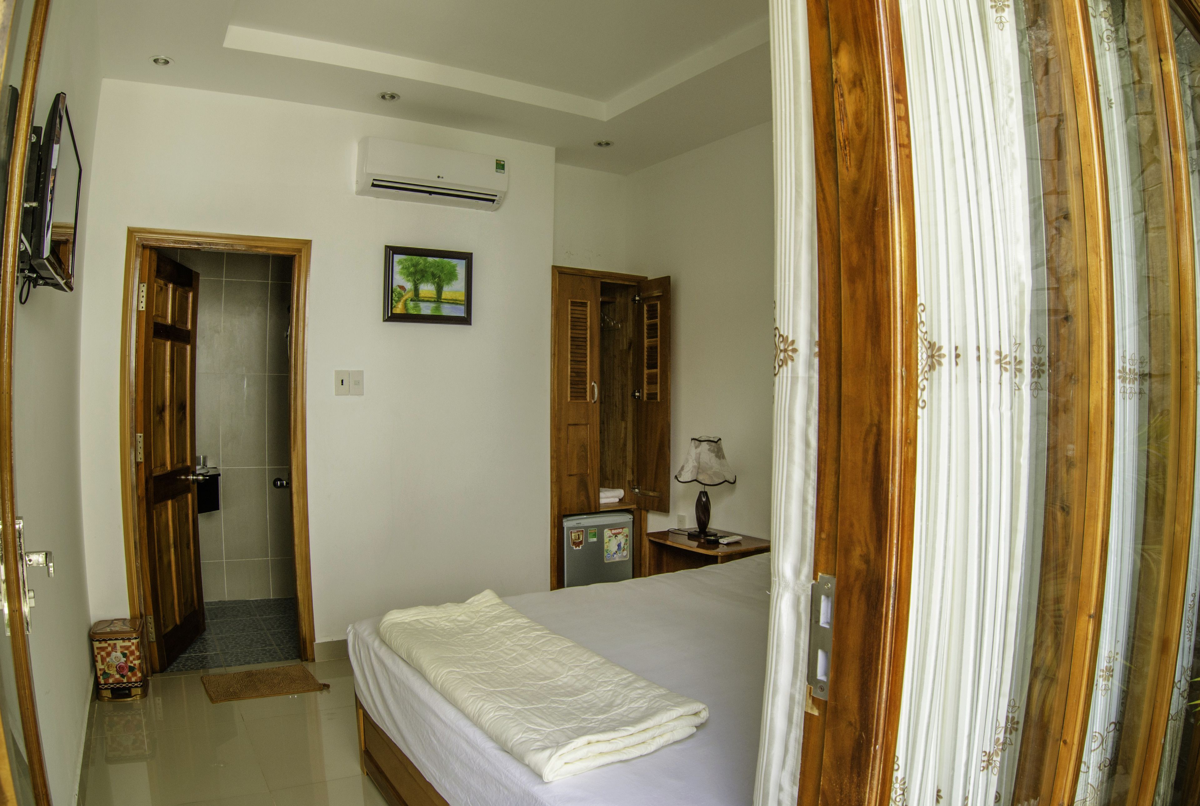 A bedroom with a bed, a wooden wardrobe, a small table with a lamp, and an air conditioning unit on the wall.