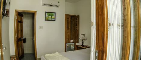 A bedroom with a bed, a wooden wardrobe, a small table with a lamp, and an air conditioning unit on the wall.