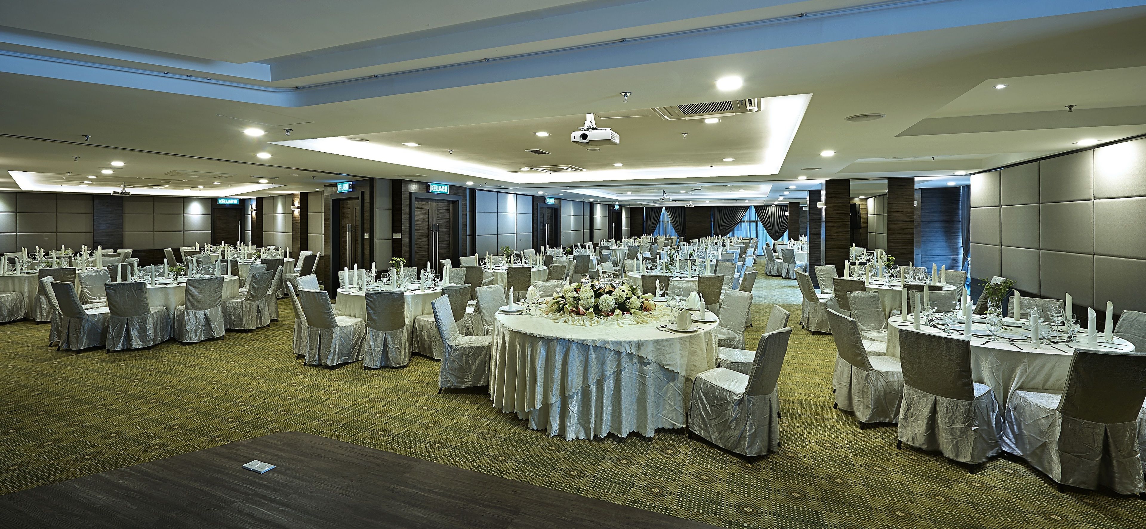 A large banquet hall with round tables, chairs, and a central floral arrangement.