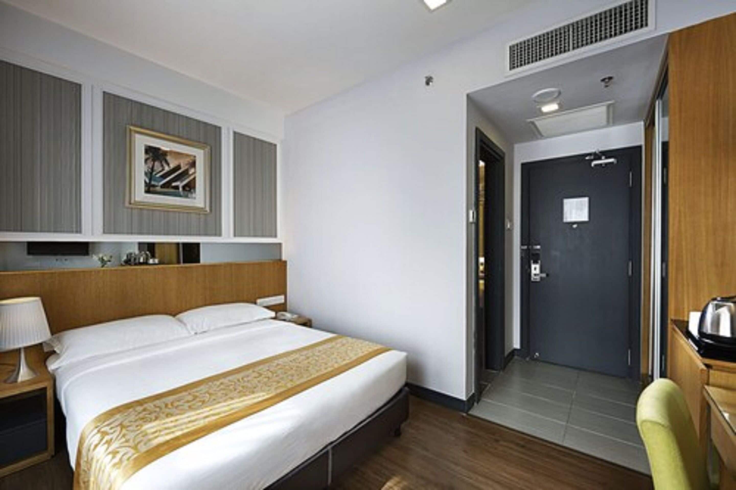 Ein Hotelzimmer mit einem großen Bett, einem Nachttisch mit Lampe, einem gerahmten Bild an der Wand und einer Tür zu einem Badezimmer.