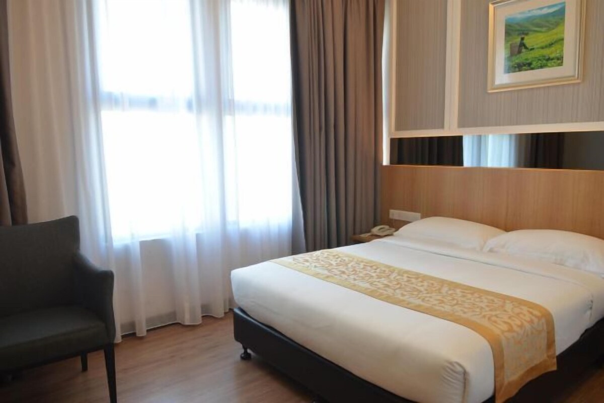 A hotel room with a bed, a chair, a bedside table, and a painting on the wall.