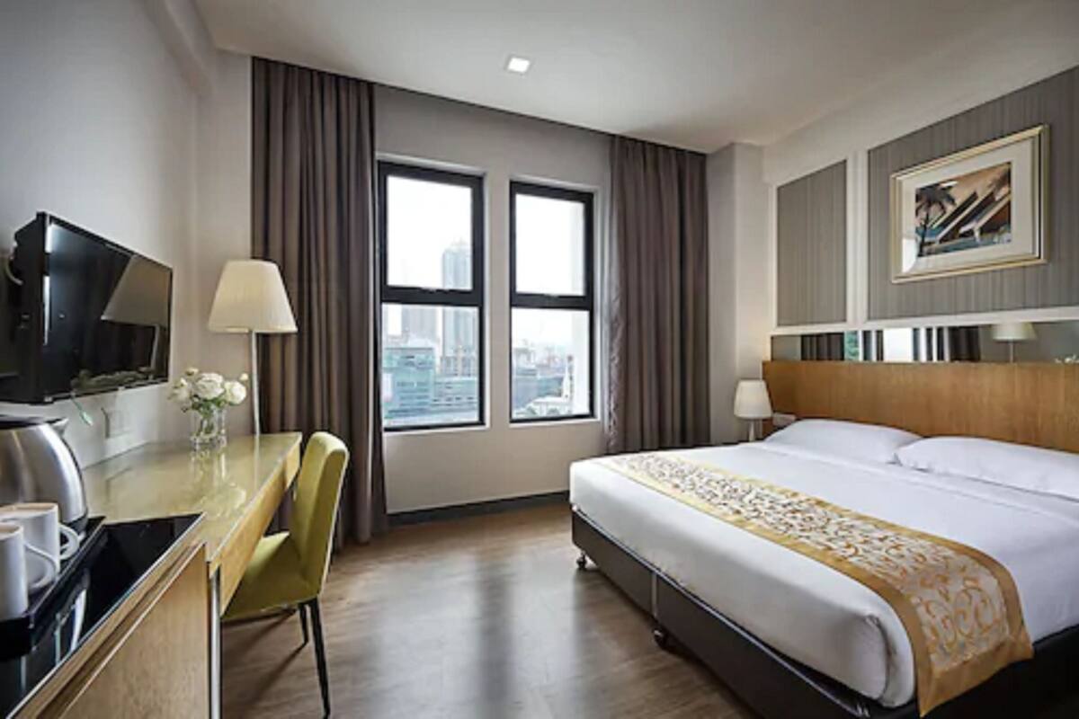 A hotel room with a bed, a desk with a chair, a TV, and a window with curtains.