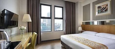 A hotel room with a bed, a desk with a chair, a TV, and a window with curtains.