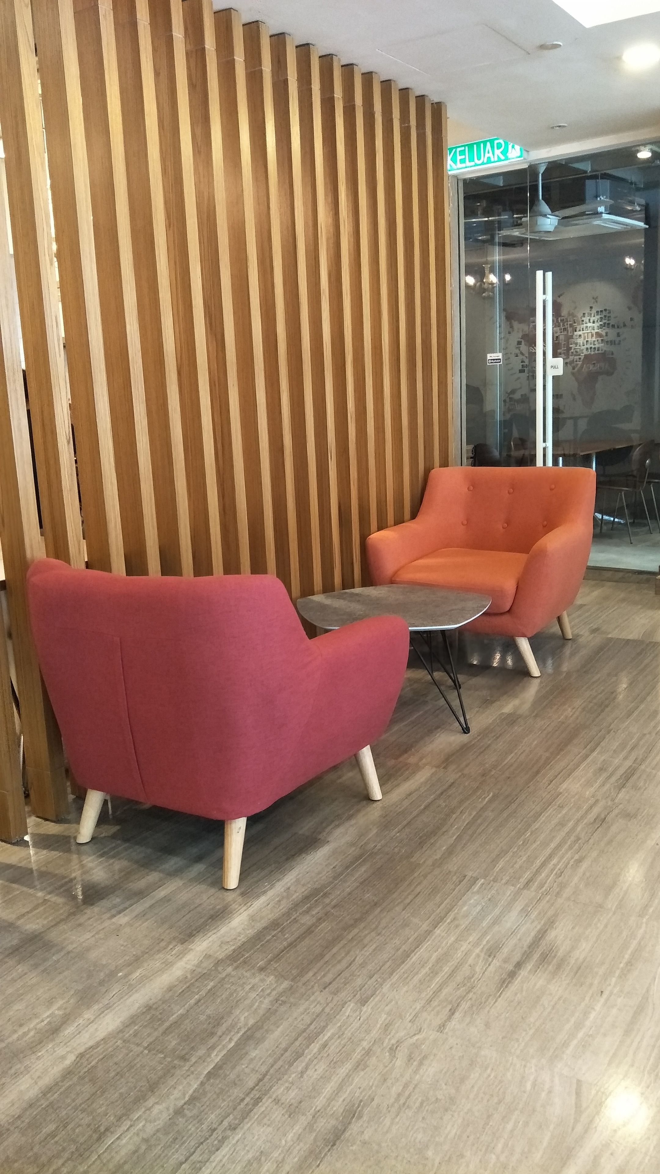 Interior moderno com dois poltronas vermelhas e uma pequena mesa, parede com ripas de madeira e porta de vidro com a inscrição 'PULL'.