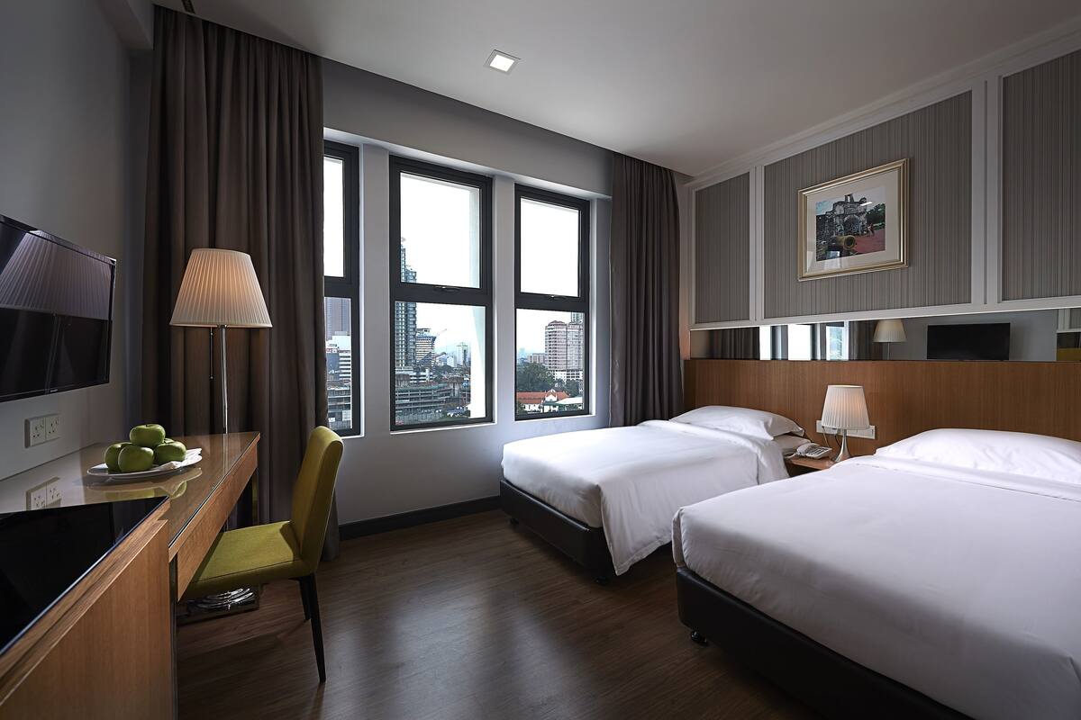 A hotel room with two beds, a desk with a TV, a chair, and a window with a city view.