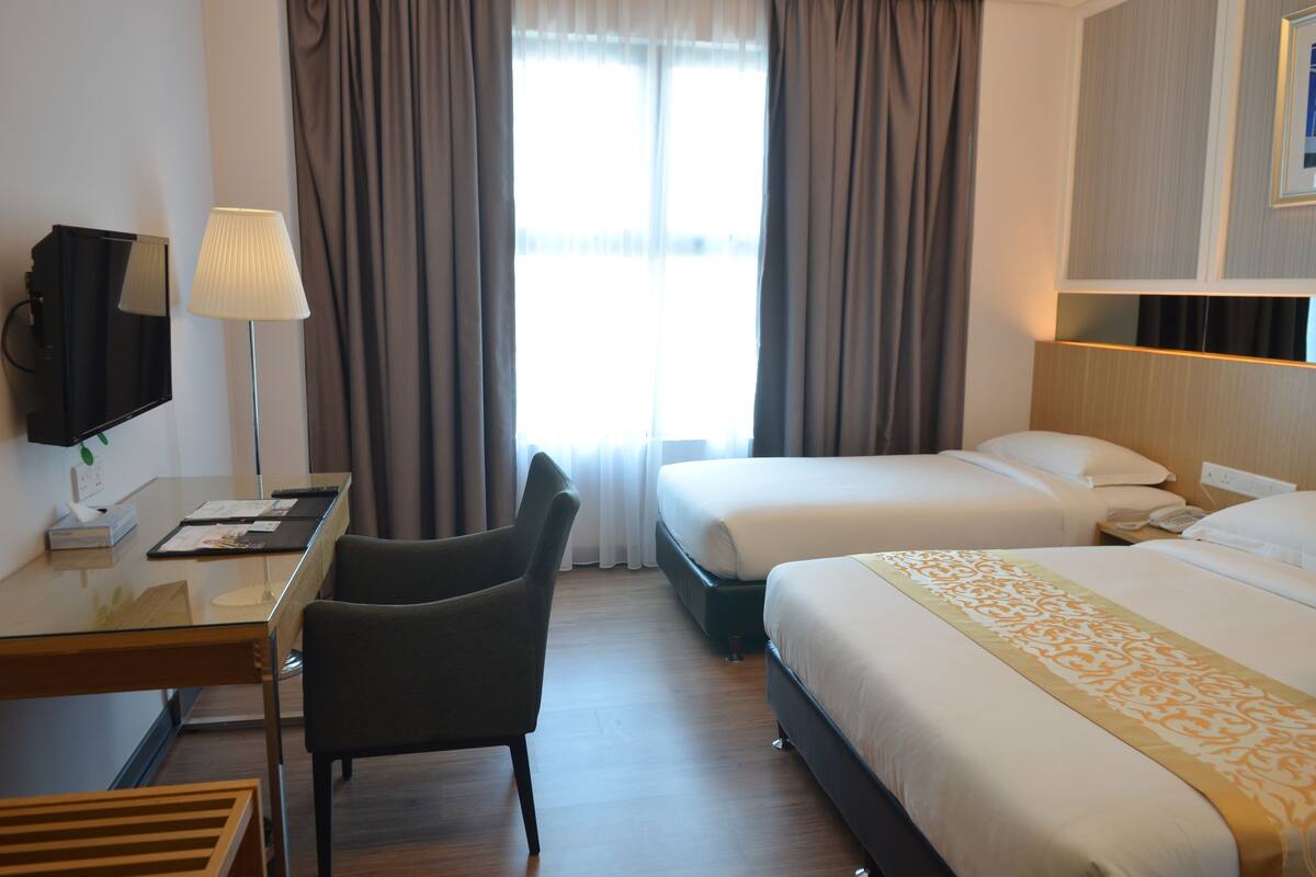 A hotel room with two beds, a desk with a chair, a TV, and a lamp.