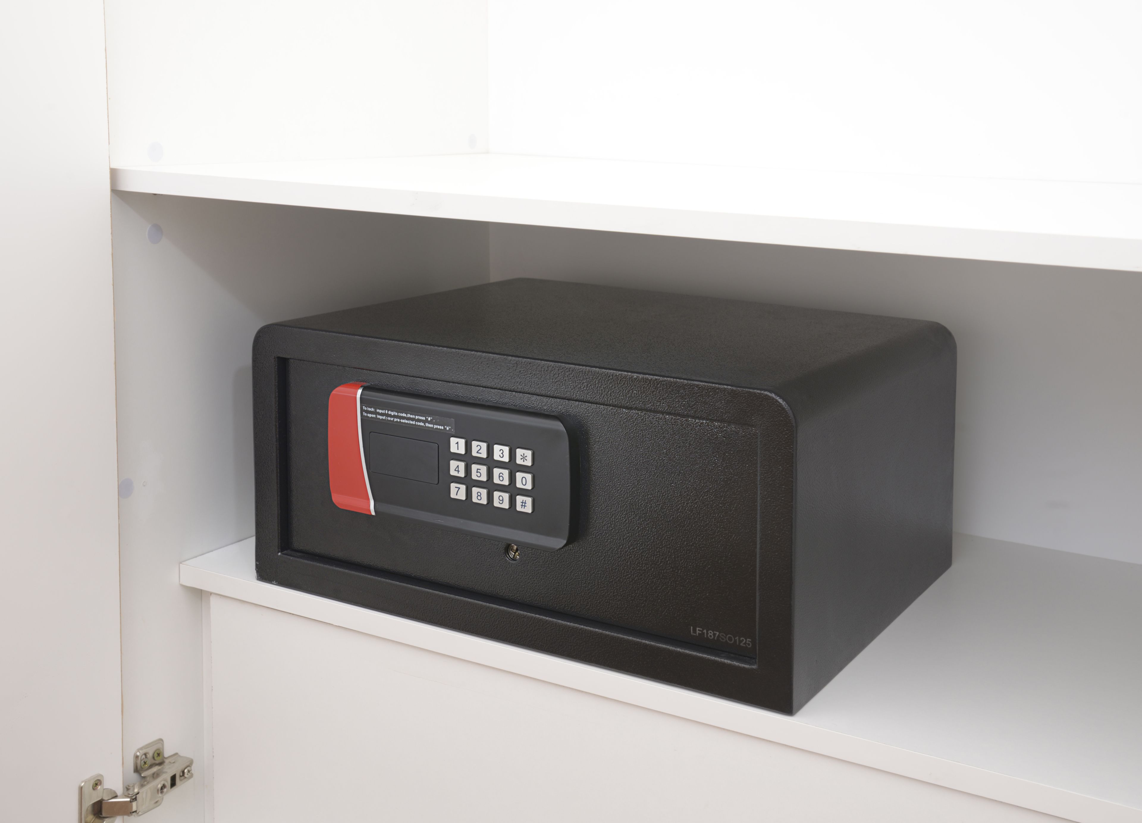 A black safe with a keypad on a white shelf.