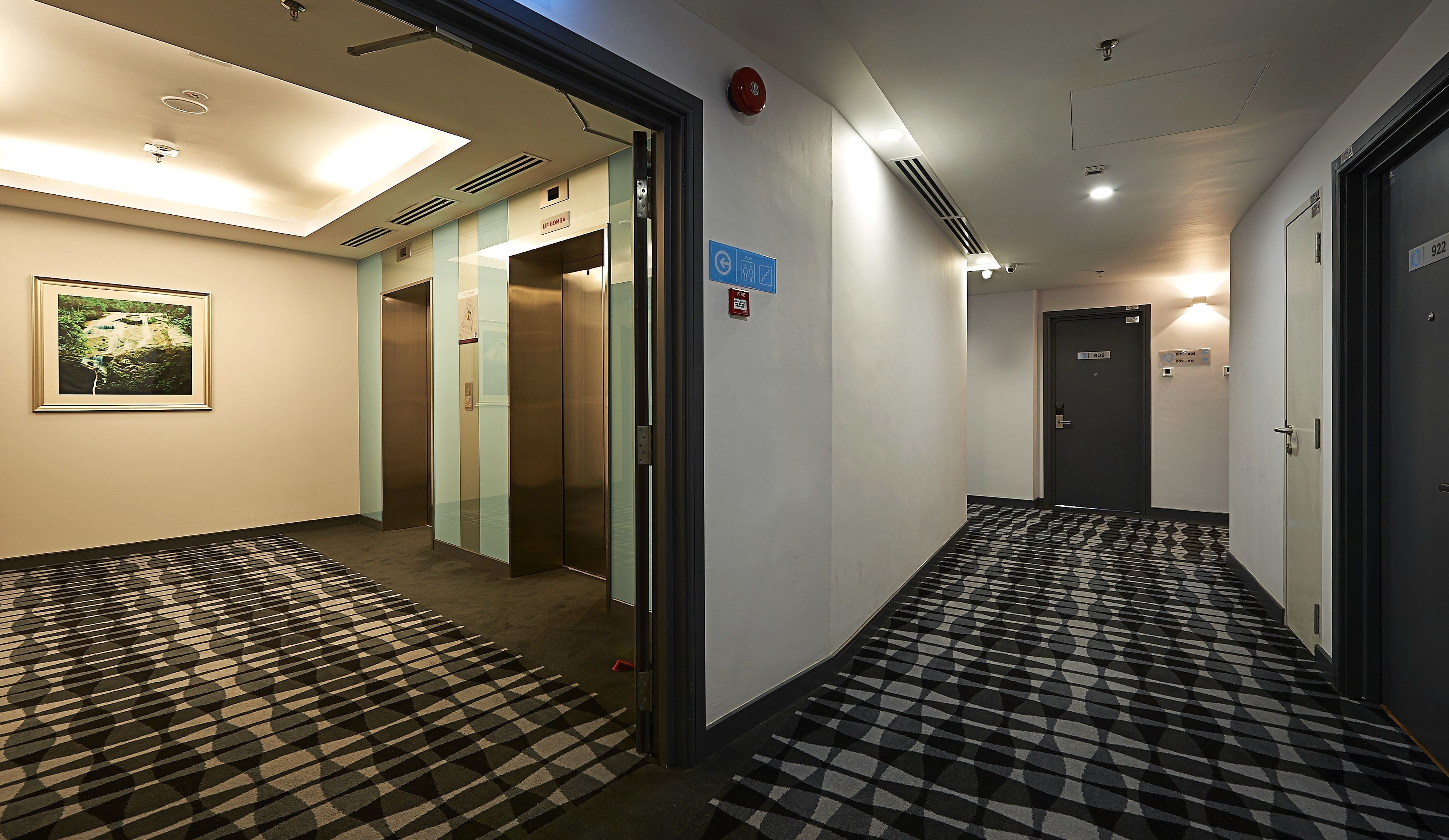 Un couloir d’hôtel avec un tapis à motifs, un tableau encadré accroché au mur, et des portes numérotées 922 et 909.