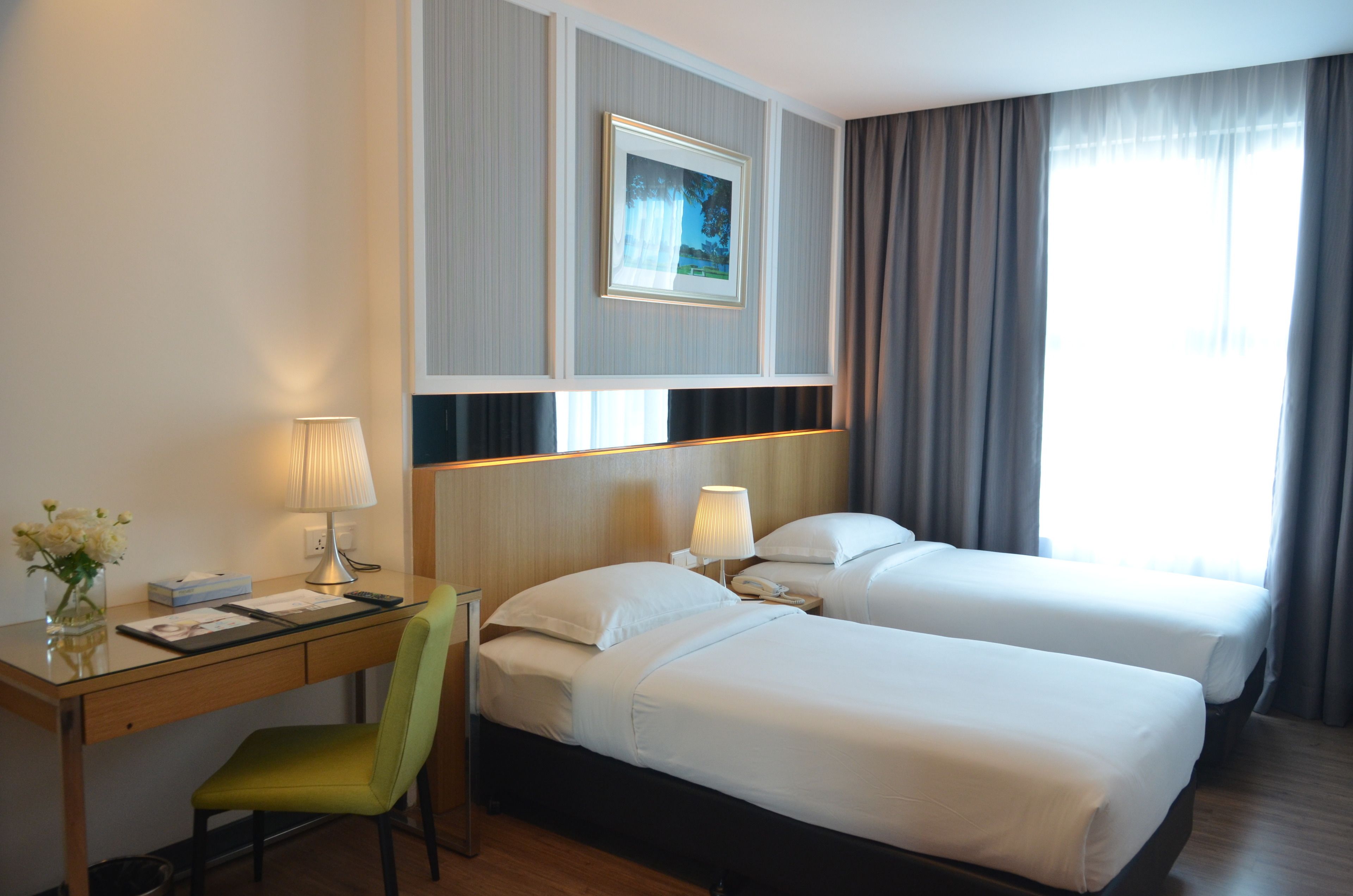 A hotel room with two beds, a desk, a chair, a lamp, and a framed picture on the wall.