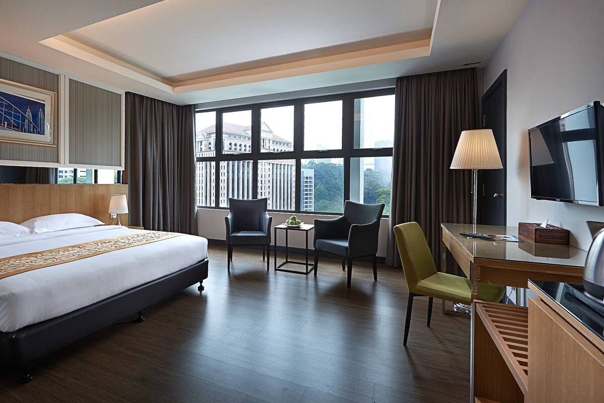 A hotel room with a large bed, a desk, a chair, a TV, and a window with a city view.