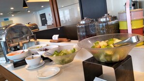 Montaje de bufé con diferentes opciones de comida, incluyendo ensaladas y un tazón de frutas variadas.