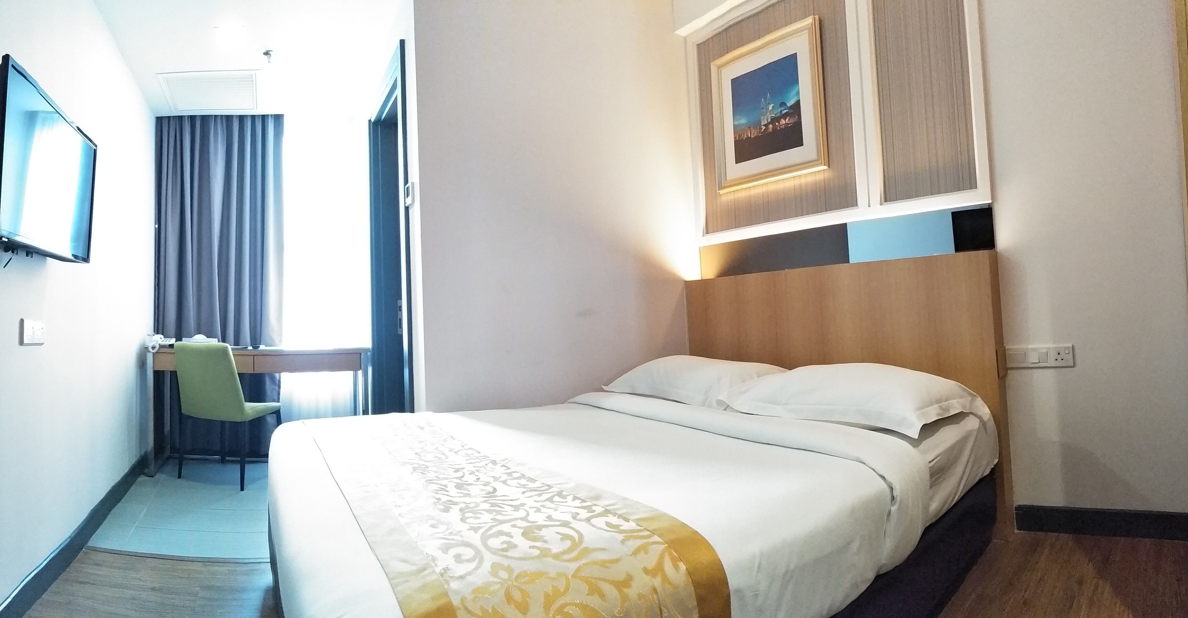Quarto de hotel com cama, escrivaninha com cadeira, televisão e um quadro na parede.