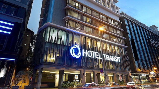 Un hotel moderno con un llamativo letrero que dice 'HOTEL TRANSIT', que presenta una estructura de varios pisos con grandes ventanales y una fachada plana.