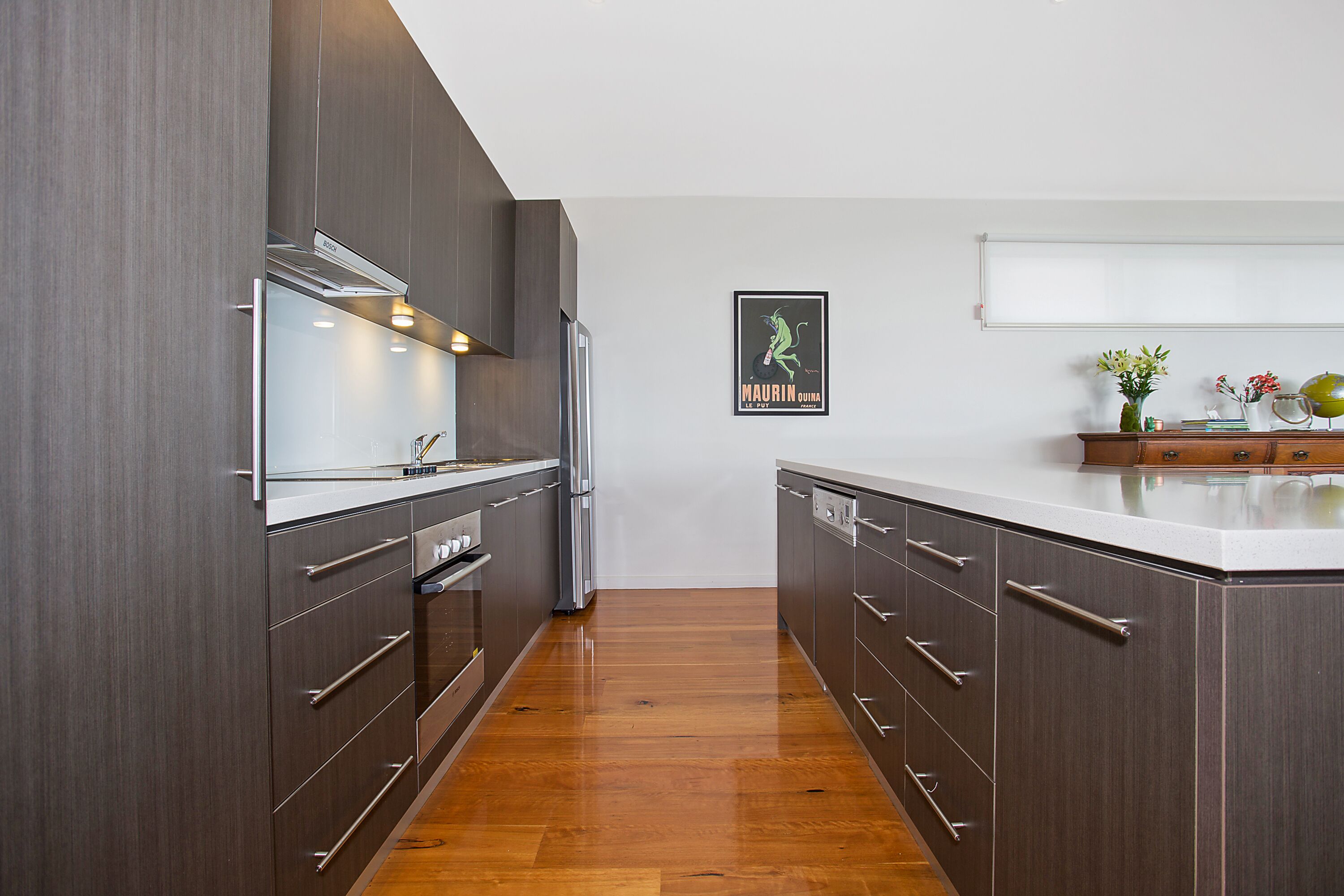 Una cocina moderna con armarios oscuros, electrodomésticos de acero inoxidable y suelo de madera.