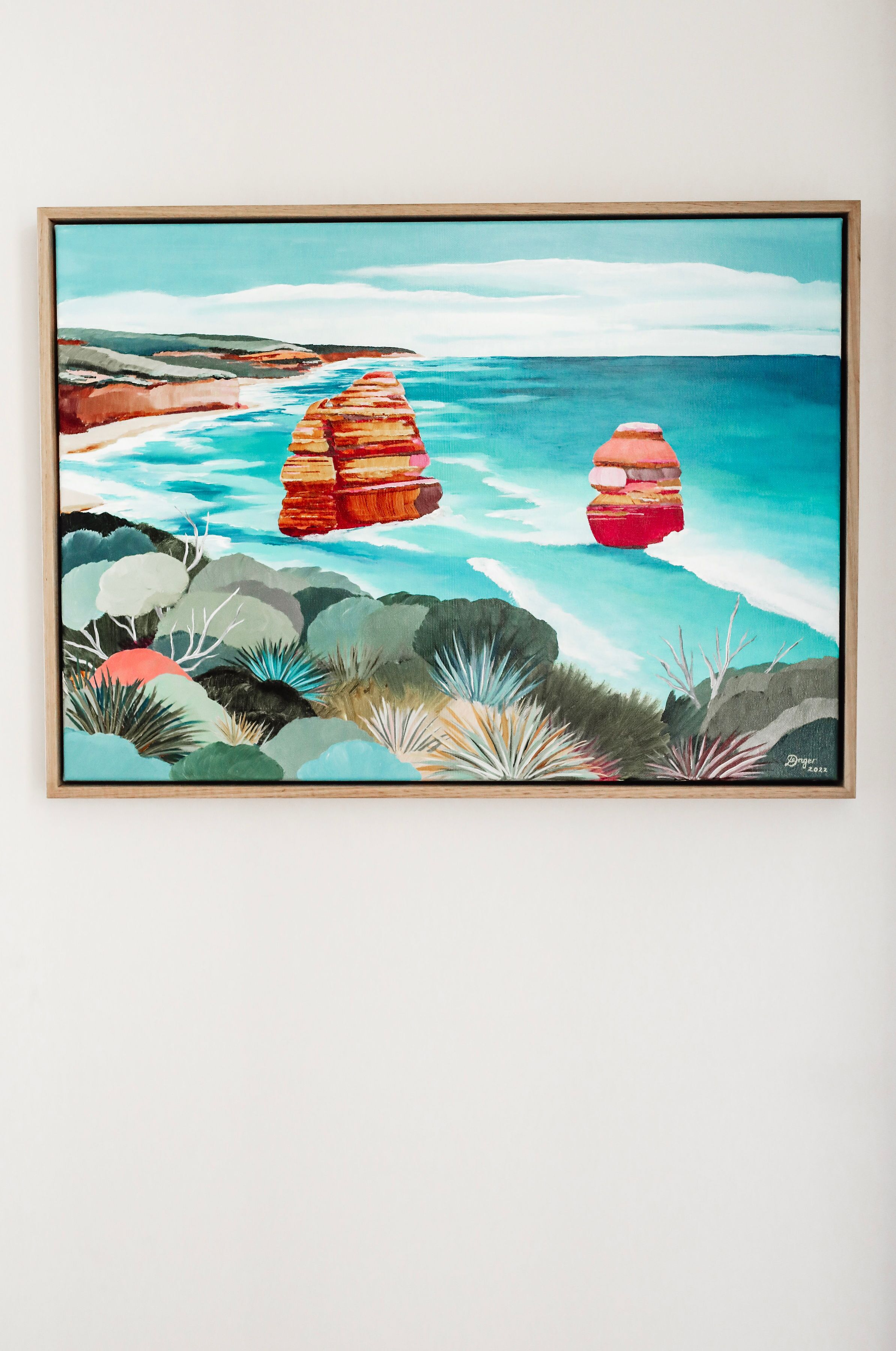 A framed painting of a coastal landscape with cliffs and waves.