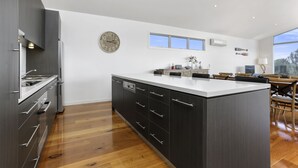 A modern kitchen with a central island, wooden flooring, and a large window providing natural light. - Anchors Beach House (Port Campbell)