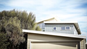 A modern two-story house with a garage, surrounded by dense vegetation. - Anchors Beach House (Port Campbell)