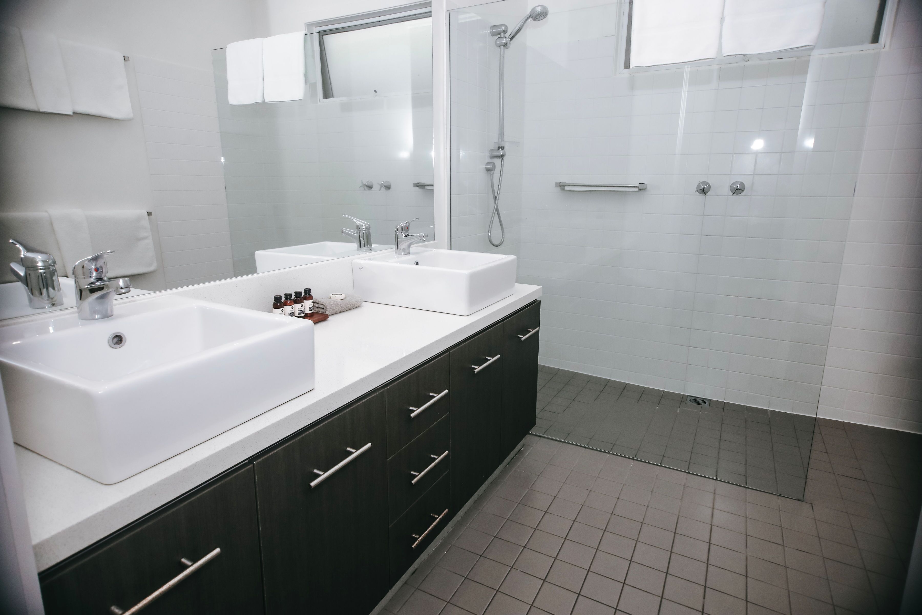 Un baño moderno con dos lavamanos, una ducha y un espejo grande.