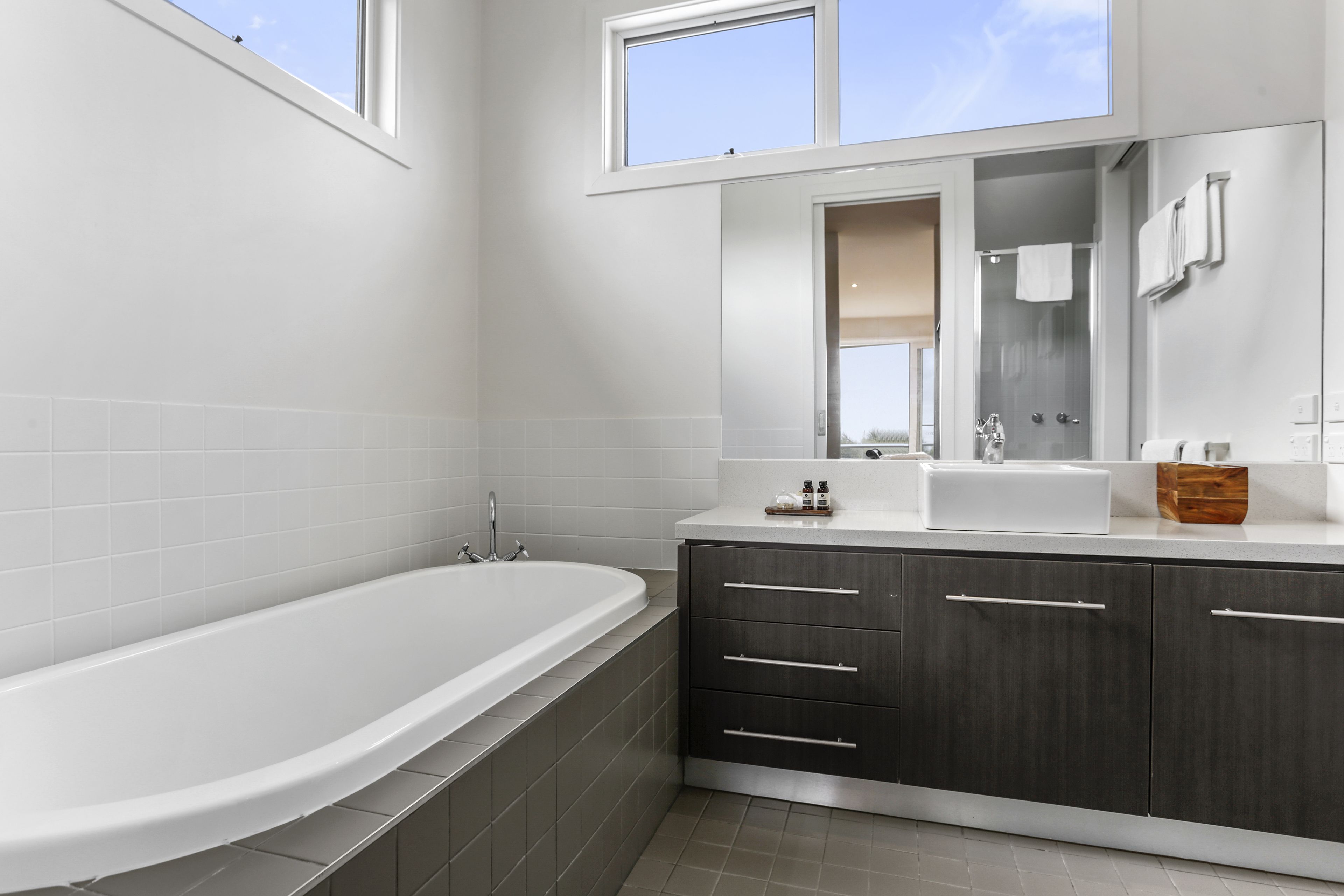 A modern bathroom with a freestanding bathtub, dark wooden cabinets, and a large mirror above the sink.