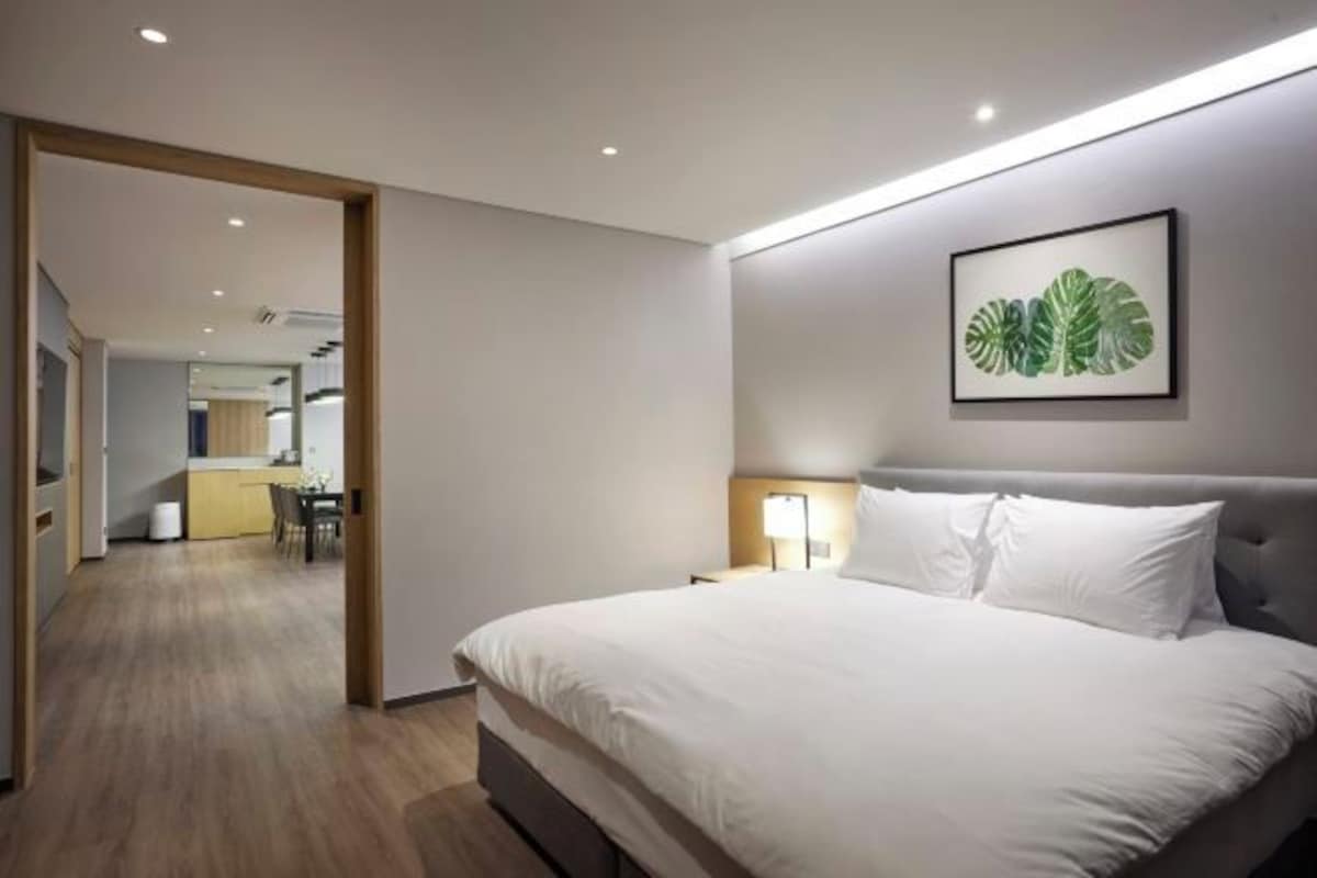 Une chambre d’hôtel moderne avec un grand lit, une table de chevet avec une lampe et une plante décorative accrochée au mur.