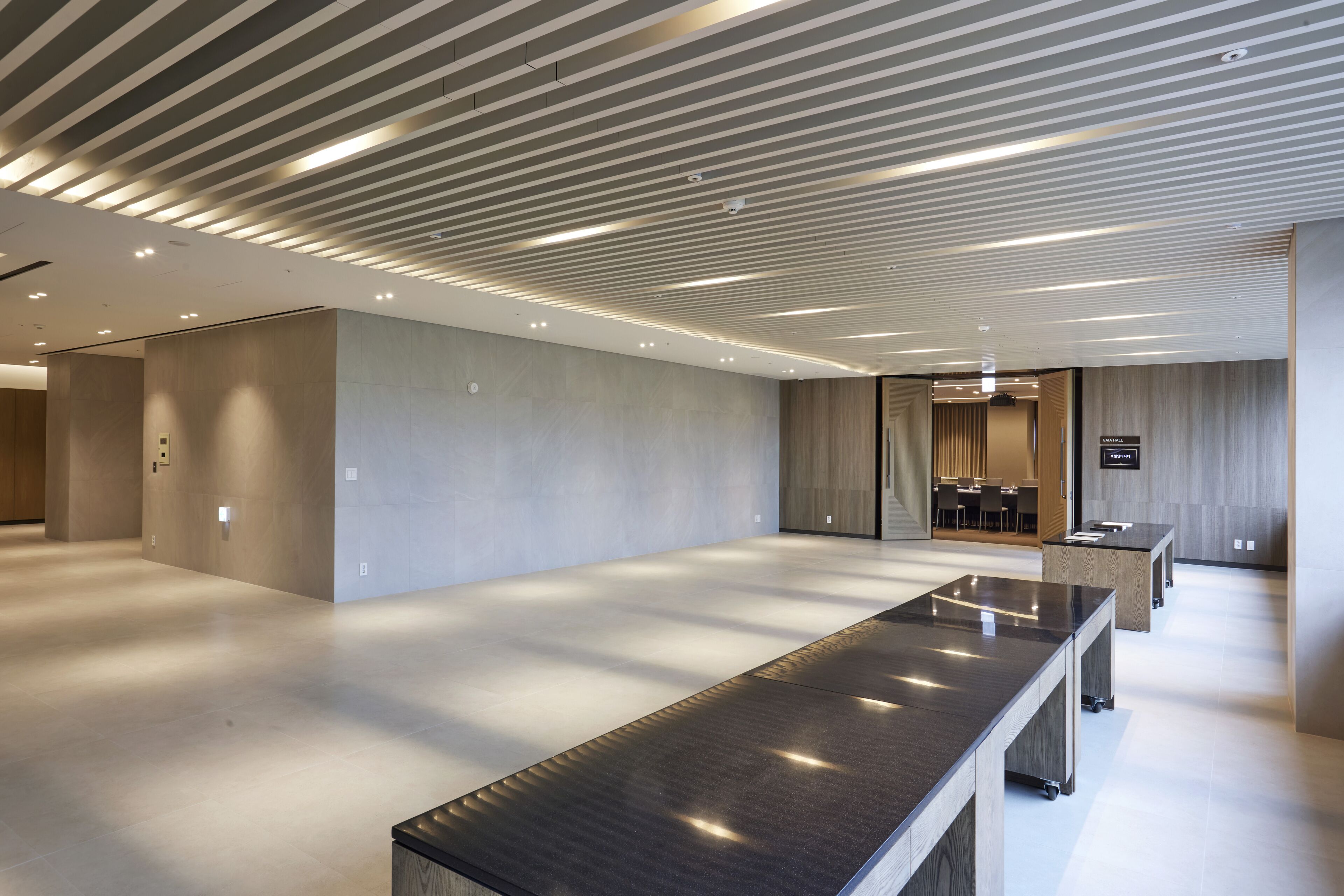 Een ruime hotel lobby met een lange receptiebalie, modern plafondontwerp en een zithoek met tafels en stoelen.