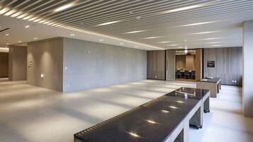 Een ruime hotel lobby met een lange receptiebalie, modern plafondontwerp en een zithoek met tafels en stoelen.